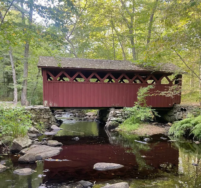 Red covered bridge over a wooded stream in Killingworth